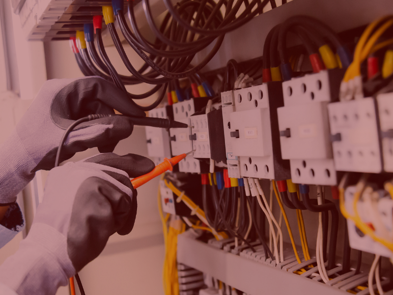 Electrician testing circuits at a distribution board with a multimeter and clipboard